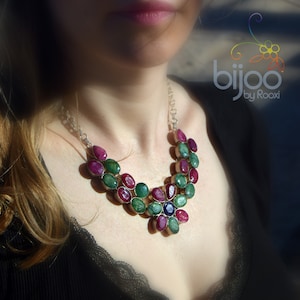 Könnte beinhalten: Eine silberne Halskette mit einem blütenförmigen Anhänger aus grünen, rosa und blauen Edelsteinen. Die Halskette trägt ein Model mit einem schwarzen Oberteil.