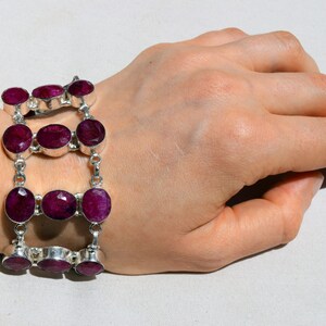 Puede incluir: Un brazalete de plata con varias filas de piedras ovaladas de color rojo oscuro. El brazalete está en la muñeca de una persona.