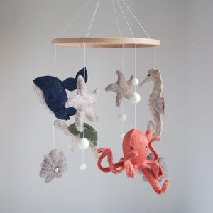 Könnte beinhalten: Ein Holz-Babymobil mit Filz-Meerestieren, darunter ein Wal, ein Seestern, eine Schildkröte, ein Oktopus und ein Seepferdchen. Das Mobile hängt an einer Holzstange.