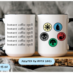 May include: White ceramic mug with black handle and rim. One side reads "instant coffee spell" repeatedly, the other features colorful symbols. The mug is 15 oz.