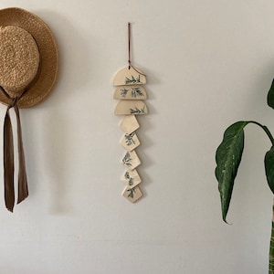 May include: A wall hanging made of wood and painted with a leafy pattern. The hanging is made of several pieces of wood in different shapes, including circles, squares, and diamonds. The hanging is attached to a brown leather cord.