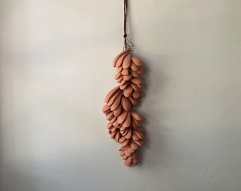Könnte beinhalten: Ein Wandbehang aus Terrakotta-Keramik mit einem kaskadierenden Design. Der Behang besteht aus mehreren kleinen, tropfenförmigen Teilen, die miteinander verbunden sind.