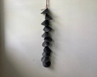May include: A black ceramic wind chime with a series of cone-shaped pieces hanging from a string.