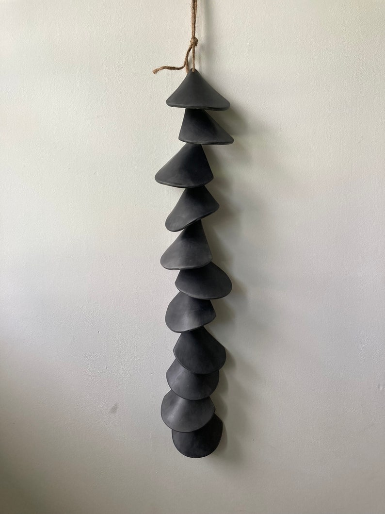 Peut inclure: Un carillon en c&eacute;ramique noire avec une s&eacute;rie de cloches coniques suspendues &agrave; une ficelle.