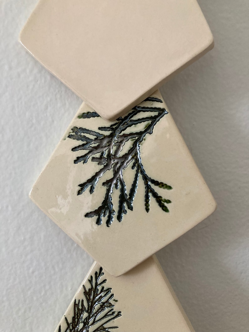 May include: Three white ceramic tiles with a diamond shape. Each tile has a black and green leafy design.