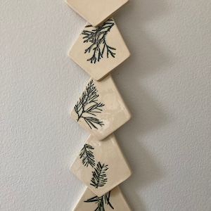 May include: A set of five ceramic diamond-shaped ornaments with a cream background and black and green leaf designs.
