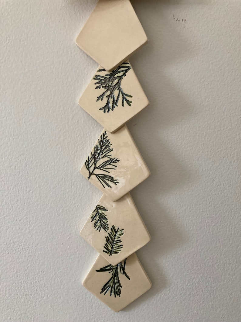 May include: A set of five ceramic diamond-shaped ornaments with a cream background and black and green leaf designs.