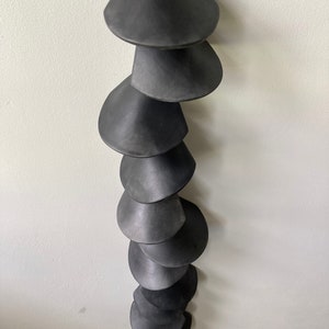 Peut inclure: Un carillon en c&eacute;ramique noire avec une s&eacute;rie de cloches coniques suspendues &agrave; une ficelle.