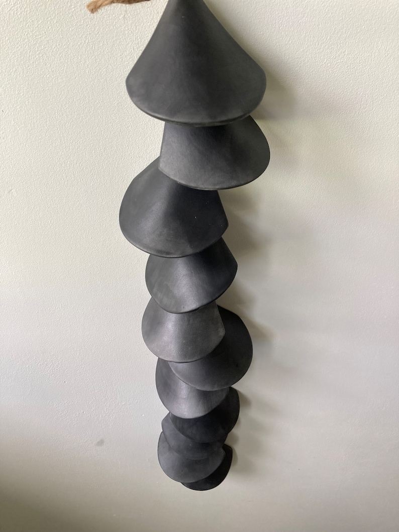 Peut inclure: Un carillon en c&eacute;ramique noire avec une s&eacute;rie de cloches coniques suspendues &agrave; une ficelle.