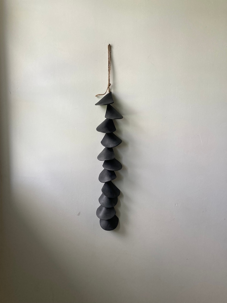 Peut inclure: Un carillon en c&eacute;ramique noire avec une s&eacute;rie de pi&egrave;ces en forme de c&ocirc;ne suspendues &agrave; une ficelle.