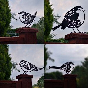 May include: Four black metal bird silhouettes mounted on wooden fence posts. The birds are in different poses, some are perched, some are flying. The birds are all facing the viewer.
