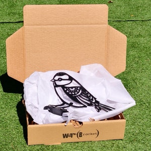 May include: A black metal bird silhouette with intricate details is packaged in a brown cardboard box with white tissue paper. The box has the text "Wot?B (bracket)" printed on the bottom.