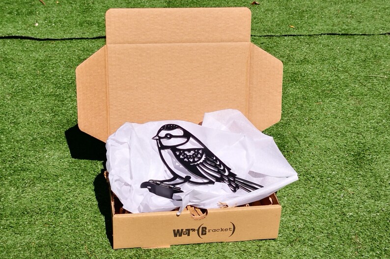 May include: A black metal bird silhouette with intricate details is packaged in a brown cardboard box with white tissue paper. The box has the text "Wot?B (bracket)" printed on the bottom.