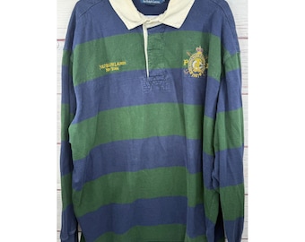 May include: A long-sleeve rugby shirt featuring wide horizontal navy blue and forest green stripes. The shirt has a cream-colored collar, a button placket, and yellow embroidered text and a crest logo on the chest reading Polo Ralph Lauren.
