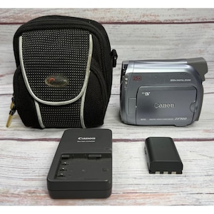 May include: A silver Canon ZR500 Mini DV digital video camcorder with 25x zoom and 800x digital zoom, accompanied by a black battery charger, a black battery pack, and a black textured carrying case with a front flap and silver trim.
