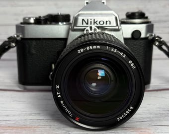Cámara réflex Nikon FE de 35 mm, color plata, con objetivo Tokina AT-X de 28-85 mm f3.5-4.5.