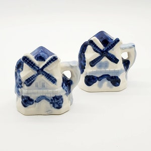 Può includere: Due saliere e pepiere in ceramica blu e bianca a forma di mulino a vento. Le saliere sono a forma di mulini a vento olandesi tradizionali con dettagli dipinti in blu e bianco.