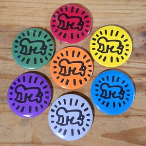 May include: Set of seven colorful round buttons featuring a black and white outline of a stick figure with a sunburst design. The buttons are red, green, yellow, orange, purple, blue, and light blue.