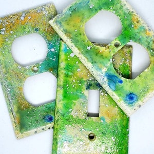 May include: Three decorative light switch and outlet covers with a green, yellow, and white marbled design. The covers have a speckled, glittery finish.