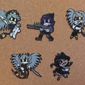 May include: A set of five enamel pins featuring cartoon characters from Murder Drones. The pins depict four winged robotic figures with yellow glowing eyes and one character with purple hair holding a large rifle, all rendered in a stylized graphic art.