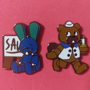 Pode incluir: Dois pinos de esmalte sobre um fundo rosa. Um pino apresenta um coelho azul com orelhas verdes e um sinal que diz "SAV". O outro pino &eacute; um urso marrom segurando uma vela.