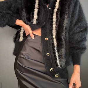 May include: A black fuzzy cardigan with white stripes and gold buttons. The cardigan is worn over a black satin skirt.