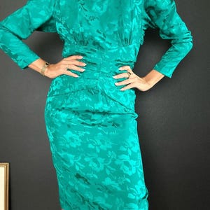 May include: A teal blue dress with a floral pattern and long sleeves. The dress has a fitted bodice and a slightly flared skirt.