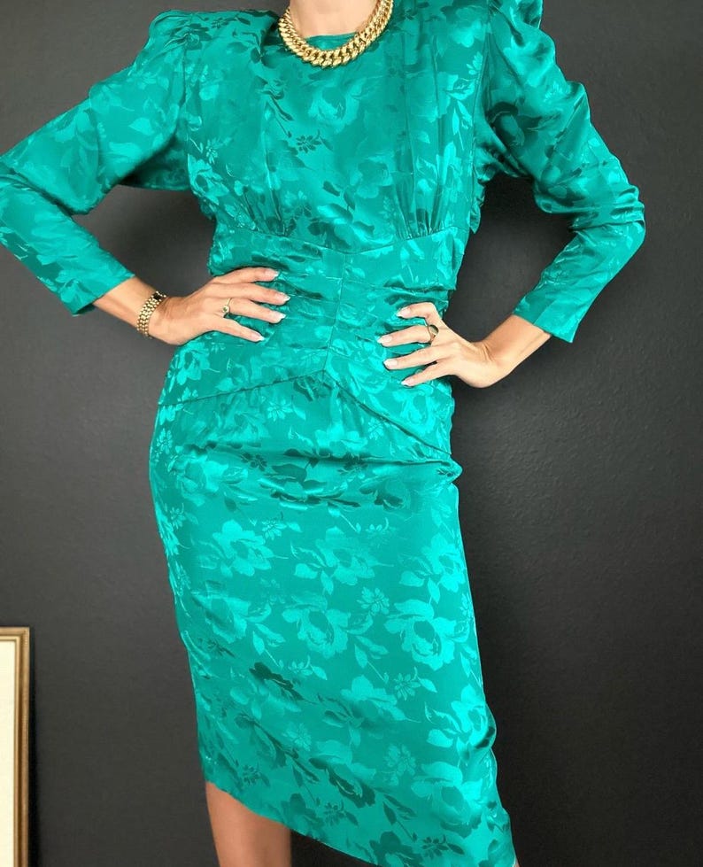 May include: A teal blue dress with a floral pattern and long sleeves. The dress has a fitted bodice and a slightly flared skirt.