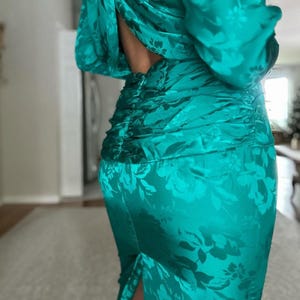 May include: A teal green satin dress with a floral pattern and a low back. The dress has a fitted silhouette and a slit in the skirt.