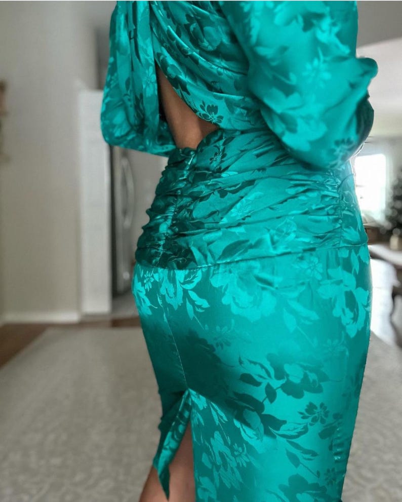 May include: A teal green satin dress with a floral pattern and a low back. The dress has a fitted silhouette and a slit in the skirt.