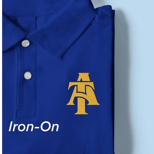 May include: Iron-on patch with the letters "AT" in a gold color on a royal blue polo shirt.