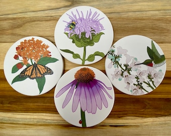 May include: Four circular coasters featuring nature illustrations. One shows a monarch butterfly on orange flowers, another a bee on a purple flower, one a hummingbird near white blossoms, and the last a purple coneflower with a small ladybug.