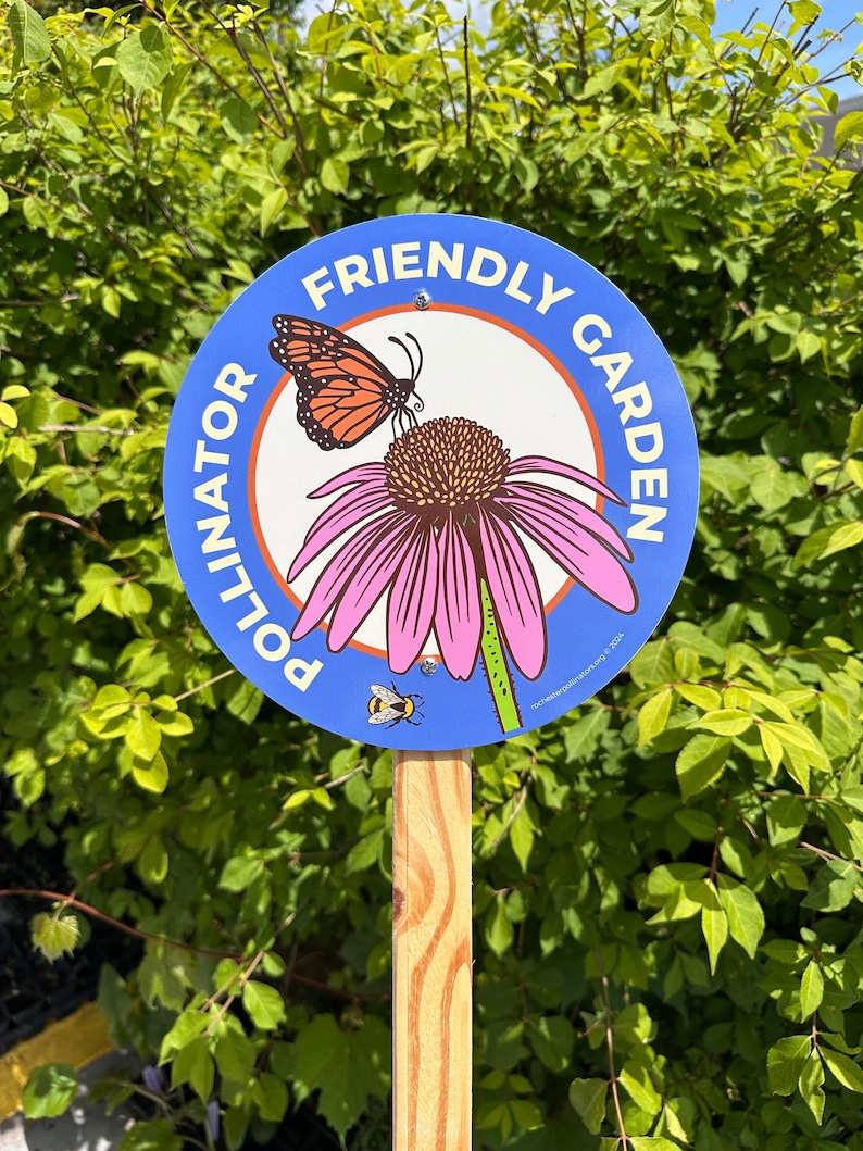 Peut inclure: Un panneau rond bleu et orange avec le texte "Pollinator Friendly Garden" et un papillon monarque et une abeille sur une fleur rose.