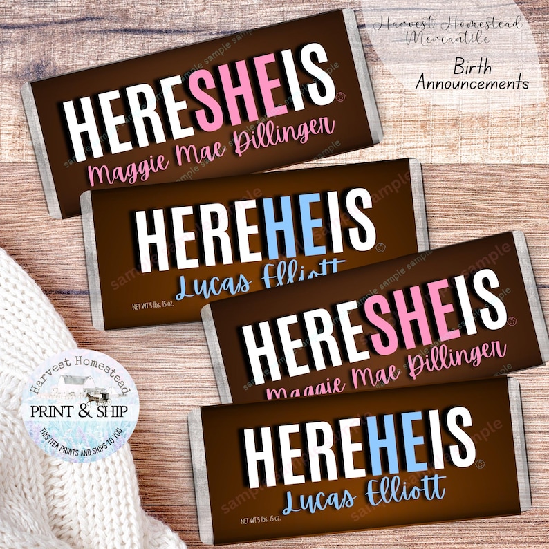 May include: Four chocolate bar birth announcements with the text "HERE SHE IS" and "HERE HE IS" in white, pink, and blue. The names "Maggie Mae Dillinger" and "Lucas Elliott" are printed on the bars. The bars are on a wooden surface.