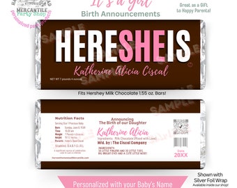 May include: A brown chocolate bar wrapper with a pink and white design. The wrapper says "Here She Is" with the baby's name "Katherine Alicia Ciscal" in pink letters. The wrapper also includes the baby's birth date, time, weight, and height. The wrapper is personalized with the baby's name and birth information.