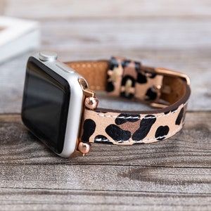 May include: A silver Apple Watch with a black and brown leopard print leather band. The band has rose gold accents.