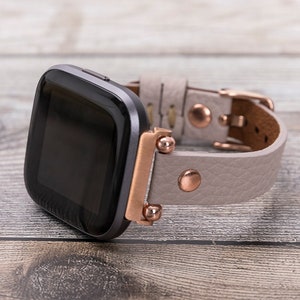 Könnte beinhalten: Ein graues Lederarmband mit roségoldenen Akzenten und einem schwarzen Smartwatch-Zifferblatt.