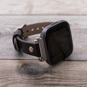 May include: A black leather watch band with a silver buckle and a black smartwatch with a touch screen.