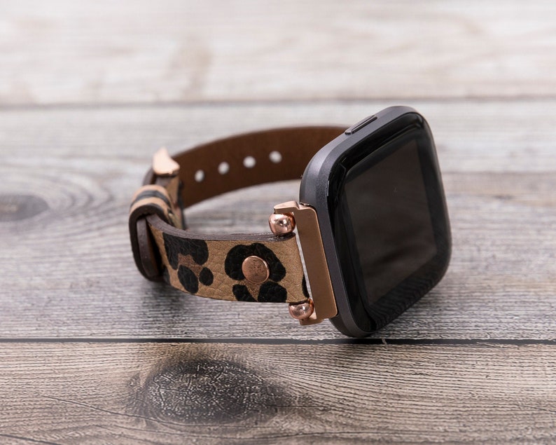 Puede incluir: Un reloj inteligente negro con una banda de estampado de leopardo marr&oacute;n y negro. La banda tiene detalles en oro rosa.