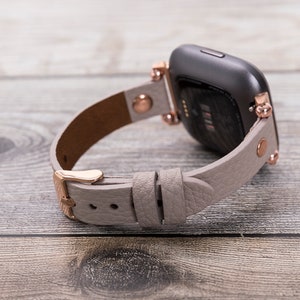 May include: A gray leather watch band with rose gold hardware and a black smartwatch face.