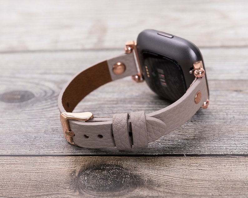 May include: A gray leather watch band with rose gold hardware and a black smartwatch face.