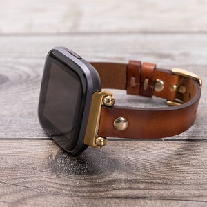 May include: A black smartwatch with a brown leather band and gold accents. The band has stitching details and a gold buckle.