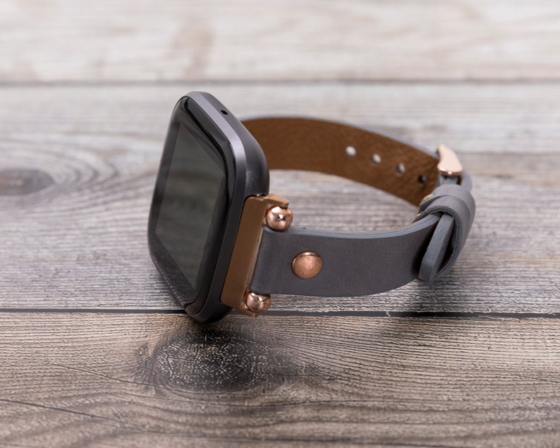 May include: A black smartwatch with a gray leather band and rose gold accents. The band has a buckle closure.