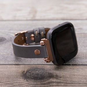 May include: A gray leather watch band with rose gold accents and a black smartwatch face.
