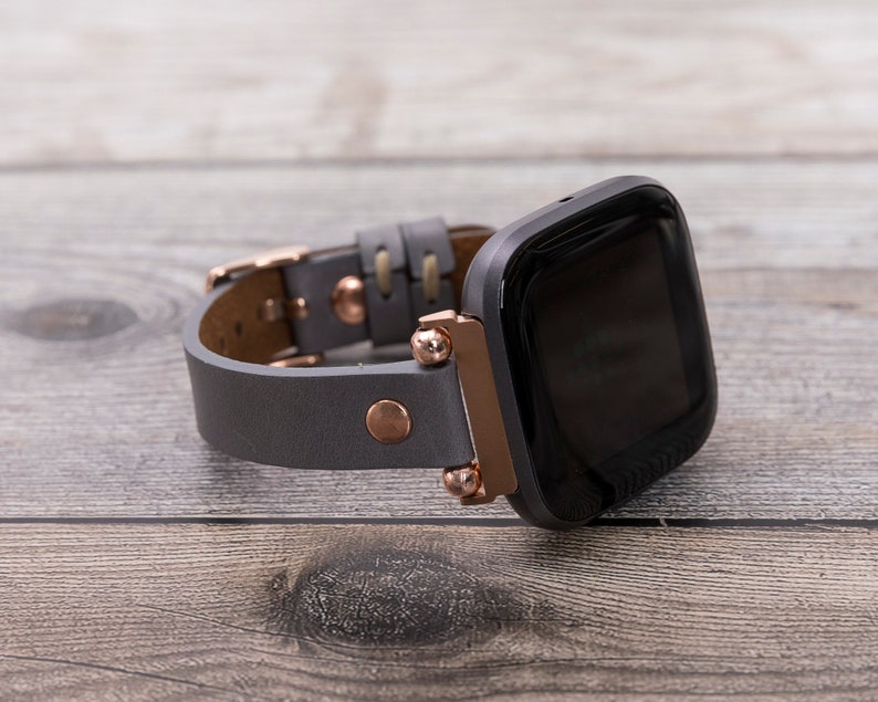 May include: A gray leather watch band with rose gold accents and a black smartwatch face.