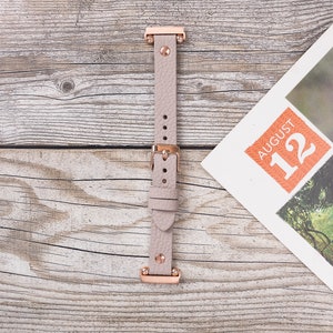 May include: A light pink leather watch band with rose gold hardware. The band has a buckle closure and is shown on a wooden surface.