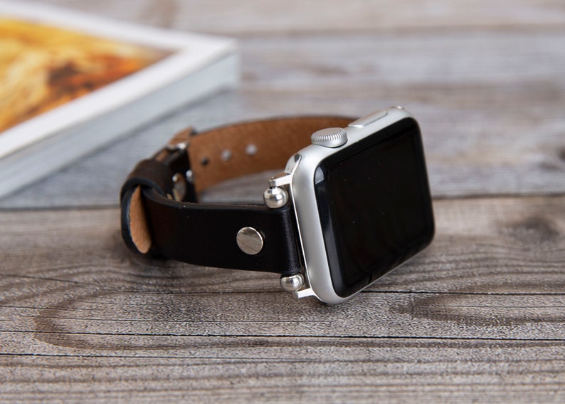 May include: A black leather watch band with silver accents and a silver Apple Watch.