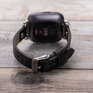 May include: A black leather watch band with a silver buckle and a silver watch face. The watch face is square and has a black background with white numbers.