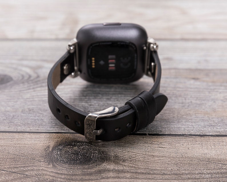 May include: A black leather watch band with a silver buckle and a silver watch face. The watch face is square and has a black background with white numbers.