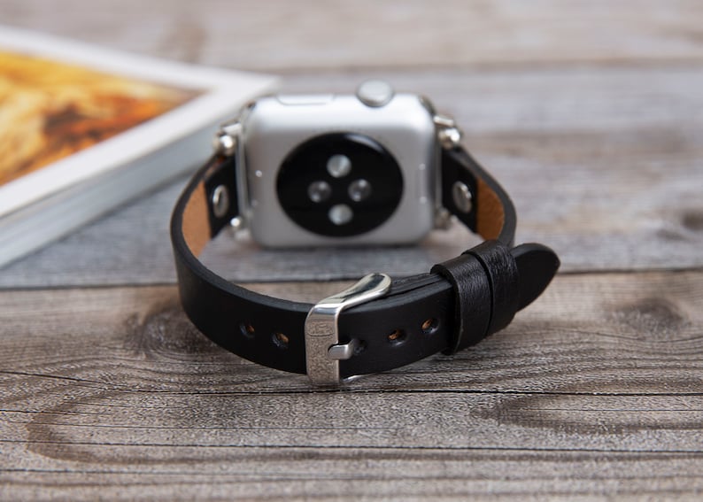 May include: A black leather watch band with a silver buckle and a silver Apple Watch face.
